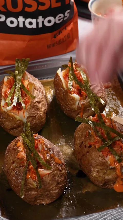 A hand laying strips of nori over the kimchi-topped baked potatoes on the baking sheet.