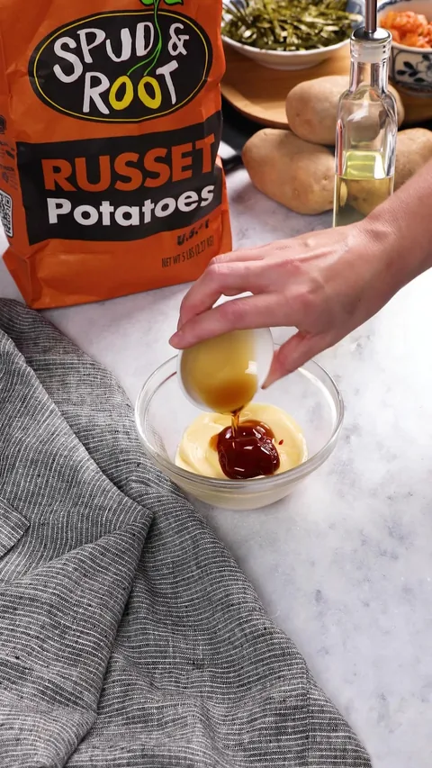A small cup tipping a light amber liquid into the bowl of mayonnaise and gochujang.