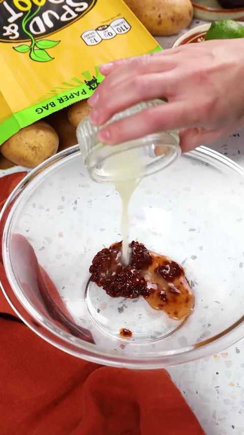 Lime juice pouring from a small glass onto minced chipotle and adobo sauce in a large glass bowl.
