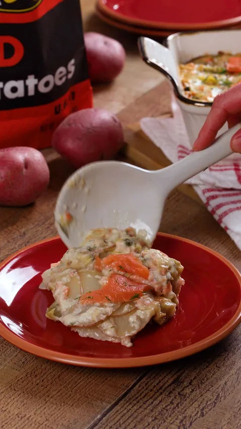 A white serving spoon lifting a slice of gratin onto a red plate.
