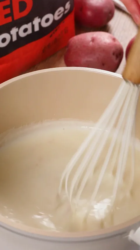 A whisk stirring a smooth white sauce in the cream pot.