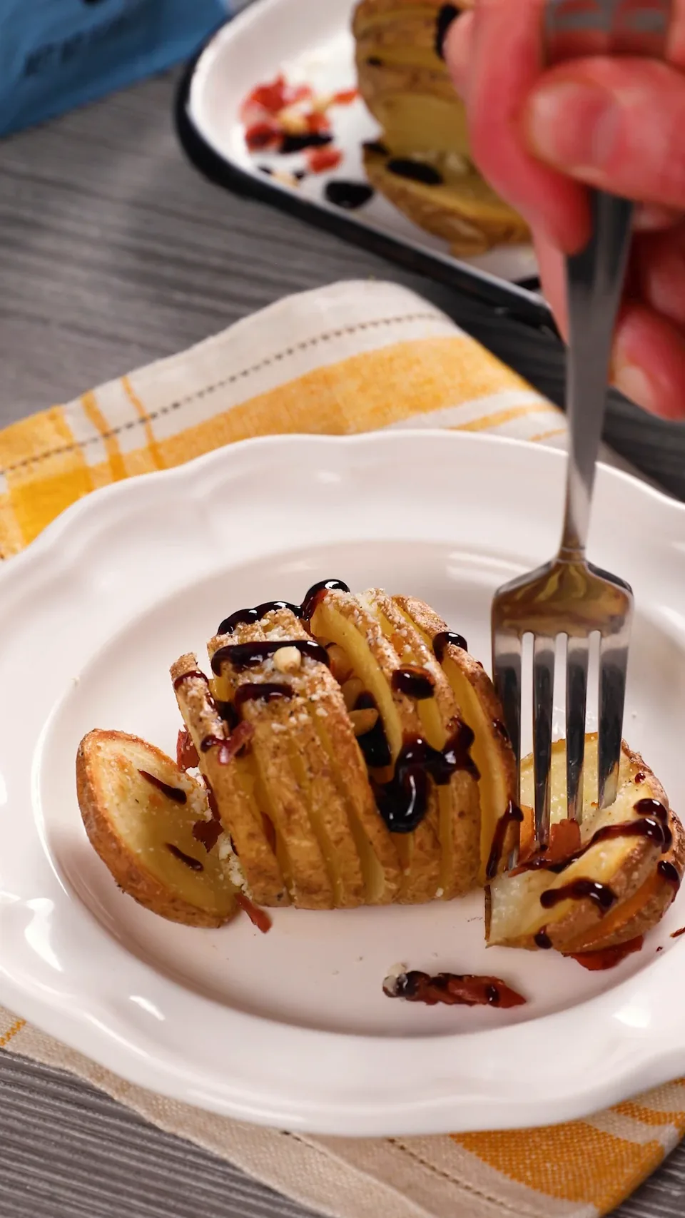A single Hasselback potato on a white plate, with a fork pulling off a slice.