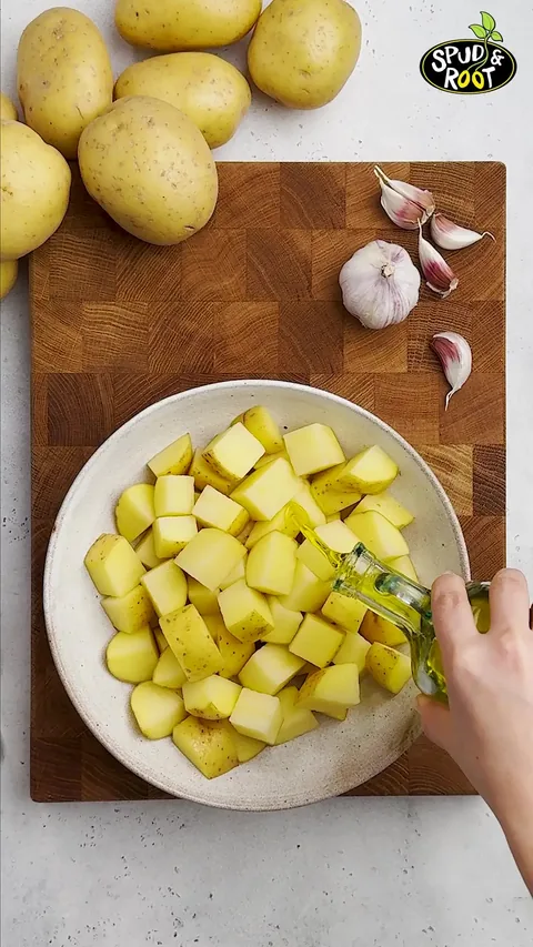 Olive oil being poured over the potato cubes in a cream bowl.