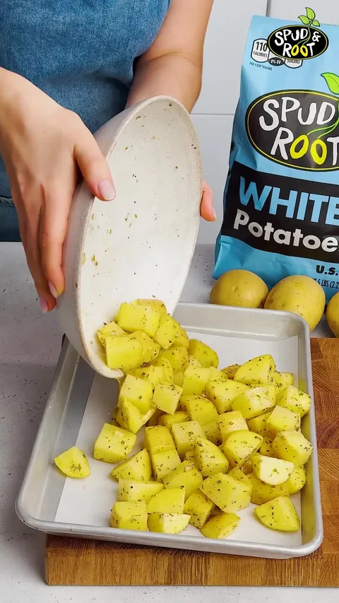 The seasoned potato cubes being tipped from the bowl onto a baking sheet, with a bag of White potatoes behind.