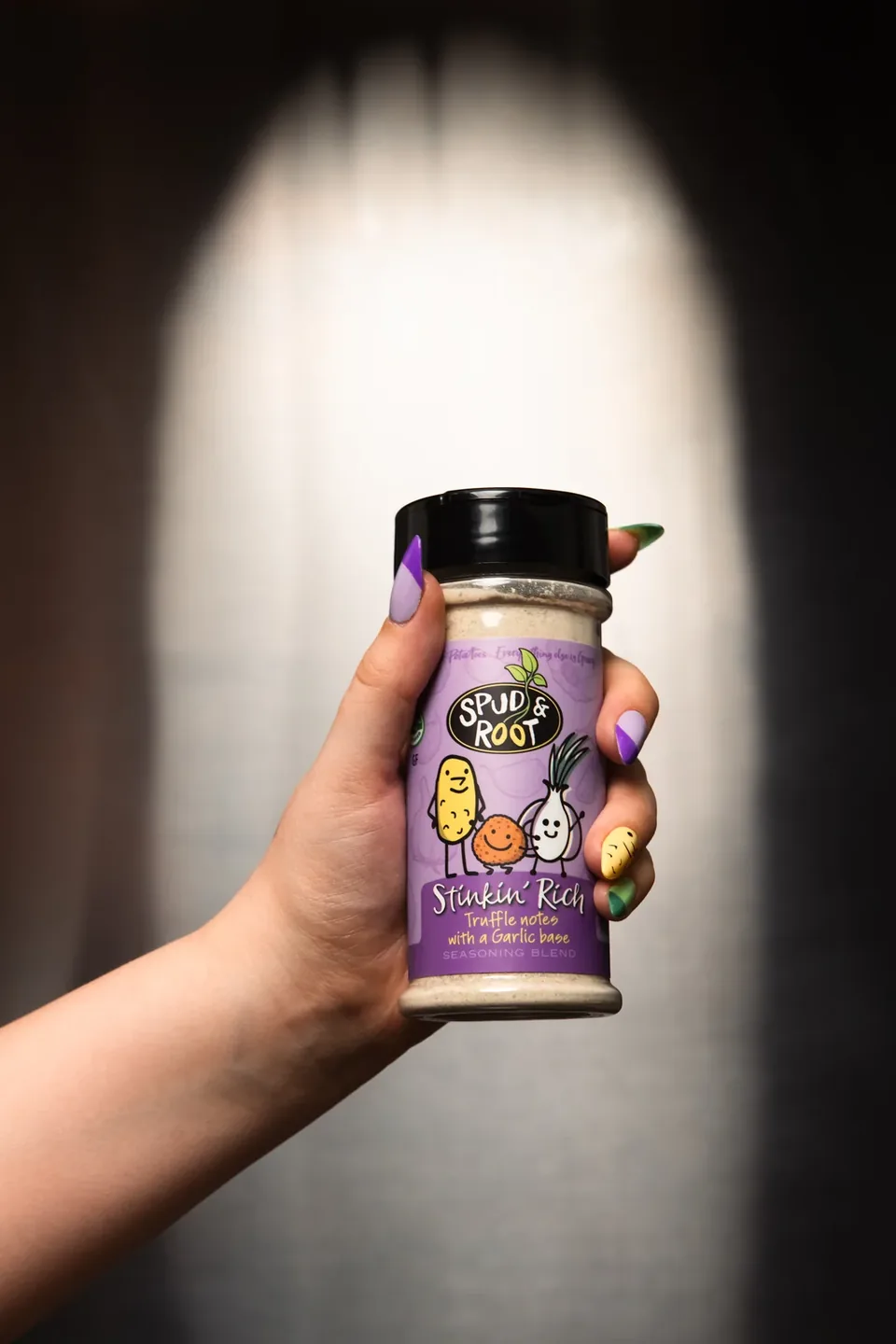 A hand holding a Stinkin' Rich jar in front of a glowing arch of light.
